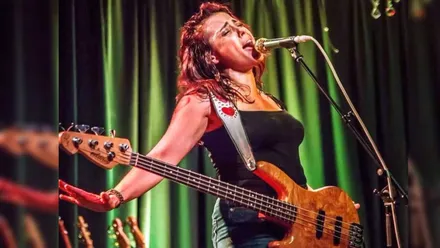 Daniel Nicole, con vestido negro, en un escenario de cortinas verdes, cantando.