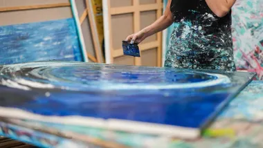 Un lienzo siendo pintado por una persona, destacan los tonos azules.