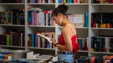 Una joven observa un libro en uno de los expositories en la Feria del Libro de Cádiz.