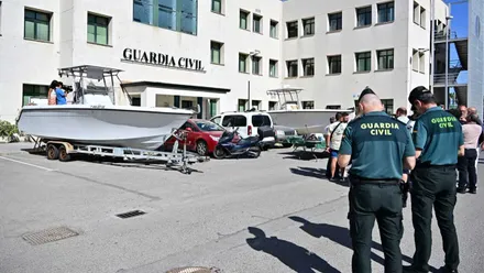 Barca de fondo en blanco con dos agentes de la Guardia Civil, con uniforme verde, en un lateral de la imagen.