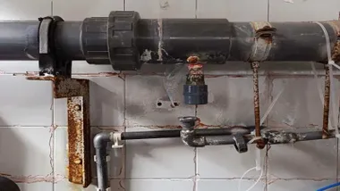 Grifo con tuberías y óxido en el Hospital de Jerez, en una pared de azulejos blancos.