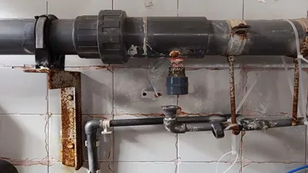 Grifo con tuberías y óxido en el Hospital de Jerez, en una pared de azulejos blancos.