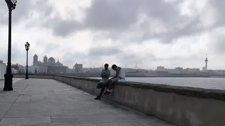 Dos conversan en la balaustrada del Campo del Sur de Cádiz con la catedral al fondo.