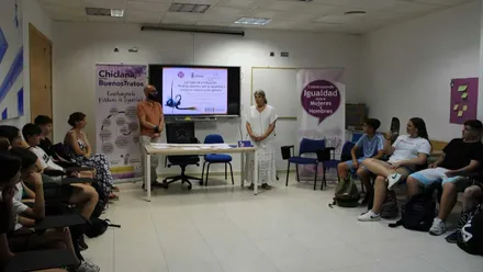 María Ángeles Martínez Rico, de Igualdad, con vestido blanco hablando a los alumnos.