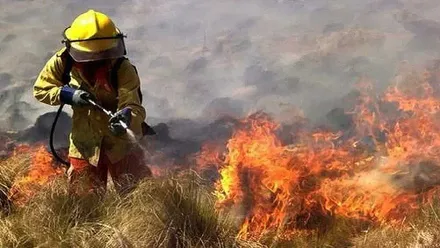 Bombero, de amarillo, sofoca las llamas que consumen una zona de pastos.
