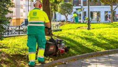 Varios jardineros cortan el césped en San Fernando con ropas verdes y amarillo fluorescente.