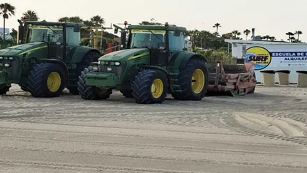 Tractores verdes que están sobre la arena, en tareas de nivelado, en la playa de La Barrosa, en Chiclana.