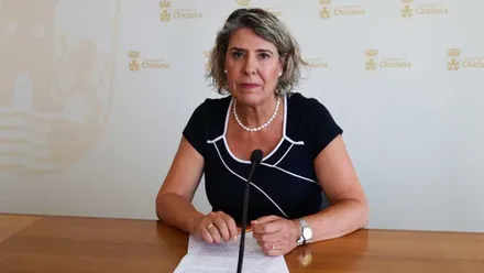 La delegada, con vestido negro y apoyada en una mesa de madera con folios en sus manos.