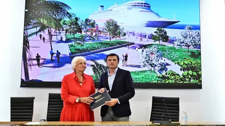 Posan Teófila Martínez, con vestido rojo, y Bruno García, tras ellos una imagen idealizada del puerto de Cádiz.