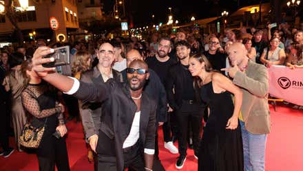 Un grupo de invitados posa para un selfi en la alfombra roja de South International Series Festival 2024, rodeado de público y fotógrafos, durante una actividad nocturna en Cádiz.