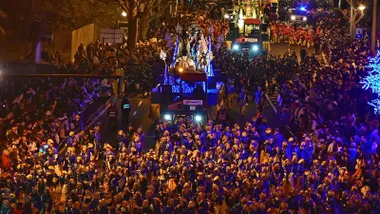 Carroza de la Cabalgata de Reyes Magos de Cádiz avanzando por una calle llena de público en la edición anterior, con decoración festiva, iluminación y personas observando el desfile desde las aceras.