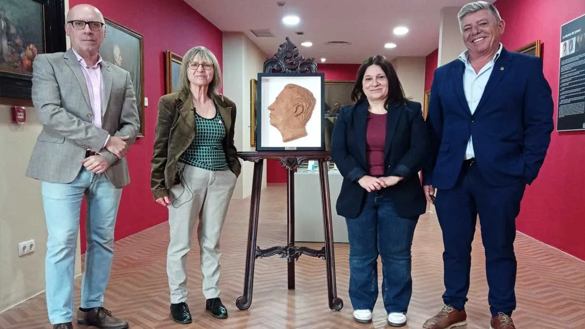 Busto de Agustín Seguro Iglesia en el centro en barro y escoltado, a ambos lados, por los representantes y la autora en un pasillo con paredes en color rojizo.