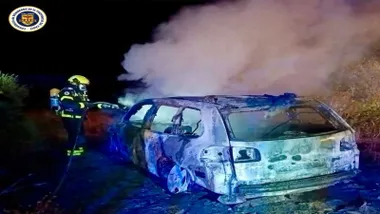Coche calcinado y bombero a su lado con un extintor trabajando sobre el fuego.