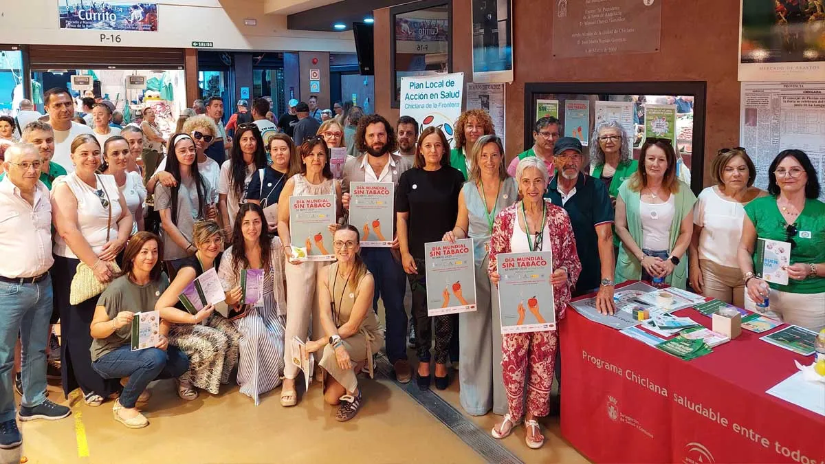Muchas personas junto a la mesa, con tapete rojo, del Día Mundial Sin Trabajo, portan en sus manos el cartel de la misma.