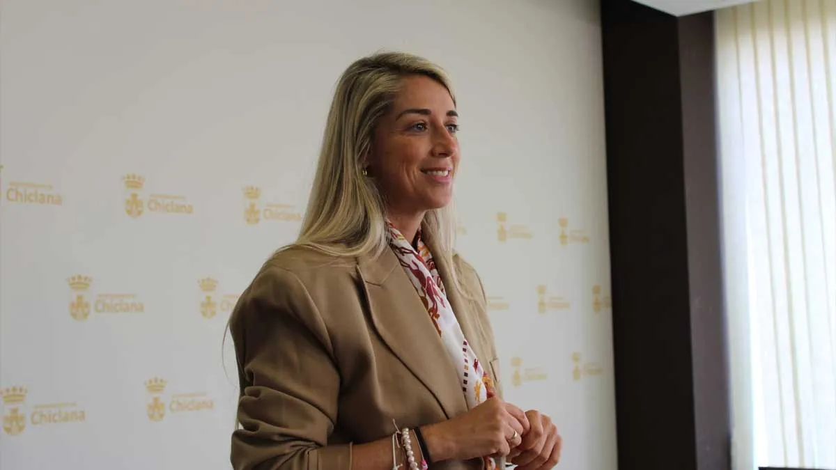 Isabel Butrón, delegada de Hacienda en Chiclana, con chaqueta beige y, tras ella, un panel blanco con el escudo de Chiclana en dorado.