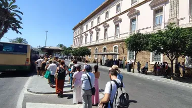 Cola a pleno sol en la Plaza de España para subir a un autobús en la octava jornada de huelga