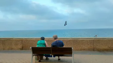 Una pareja descansa en un banco del Campo del Sur de Cádizen una imagen en la que se aprecia la humedad que se vive estos días