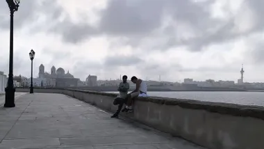 Dos conversan en la balaustrada del Campo del Sur de Cádiz con la catedral al fondo.