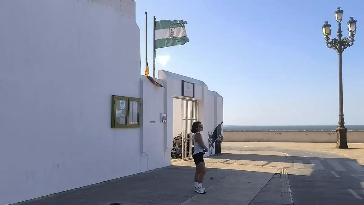 Una bandera de Andalucía ondea con fuerza por el Levante en una escuela infantil de Cádiz y una joven espera en la puerta