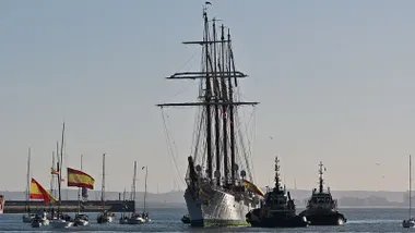Elcano llegando al puerto gaditano acompañado de pequeñas embarcaciones con banderas de España.