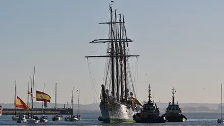 Elcano llegando al puerto gaditano acompañado de pequeñas embarcaciones con banderas de España.