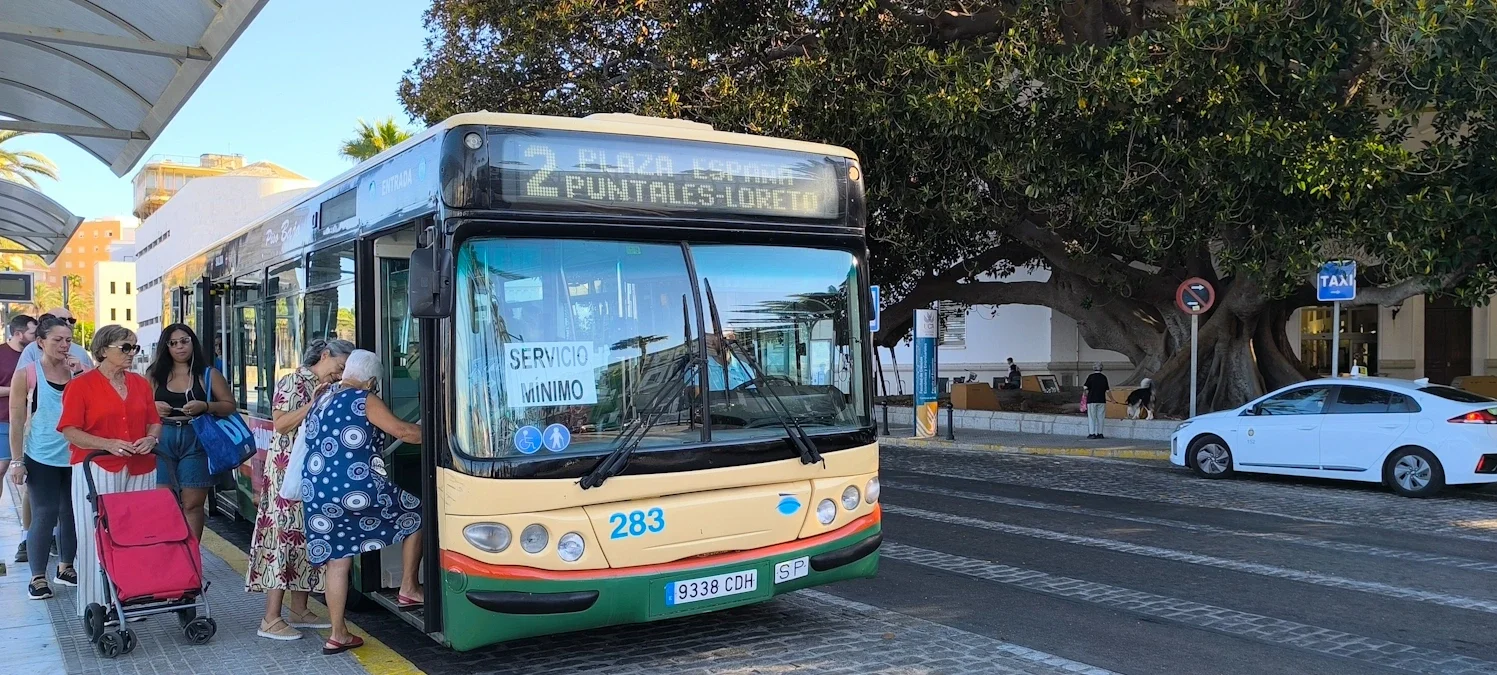 Varias personas suben al autobús de la línea 2 en la parada de La Caleta durante la huelga de autobuses con un taxi al fondo en la parada