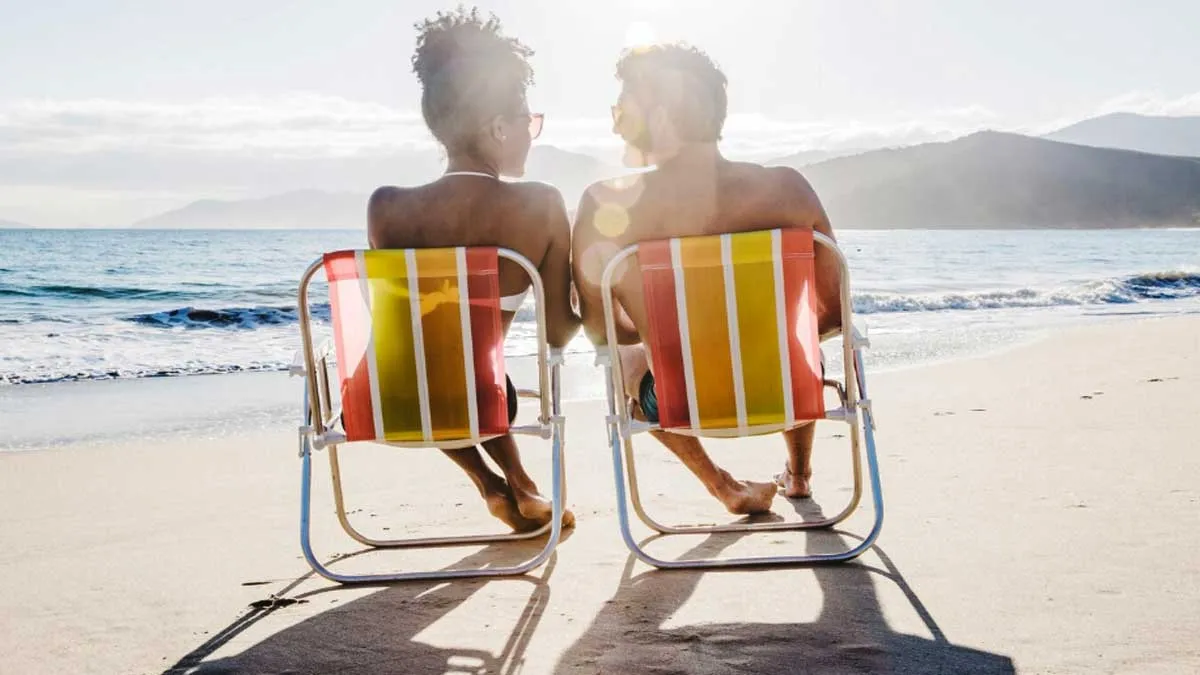 Una mujer y un hombre, sentados en una sillas amarillas y naranjas, tomando el sol a la orilla de la playa.