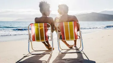 Una mujer y un hombre, sentados en una sillas amarillas y naranjas, tomando el sol a la orilla de la playa.