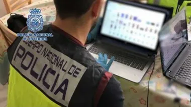 Policía Nacional, con chalequillo reflectante, delante de un ordenador portatil.