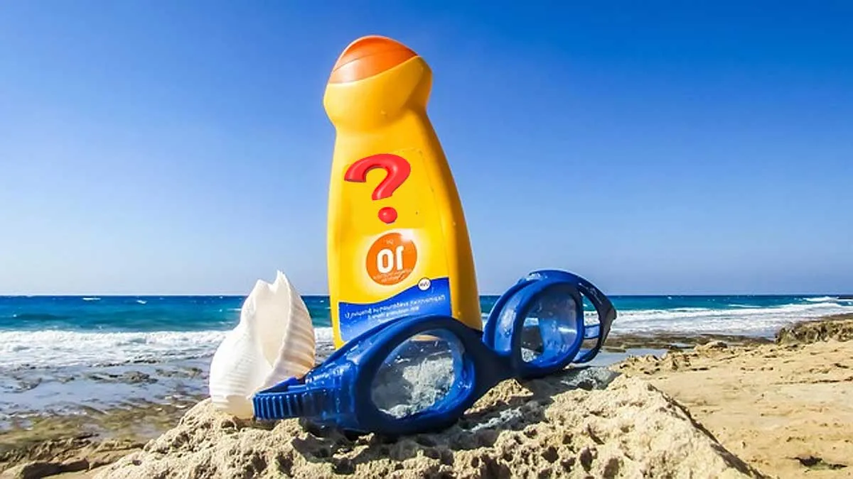 Bote de crema solar naranja en la playa junto a unas gafas de buceo en color azul.