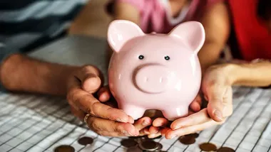 Hucha con forma de cerdito rosado sostenido por diferentes manos.