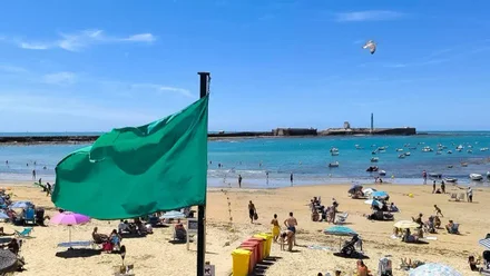 Vista de la playa de La Caleta en Cádiz con la torre de vigilancia y la bandera verde ondeando, señal de que el baño está permitido.