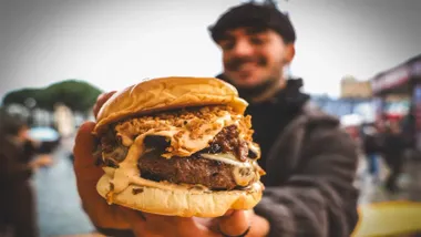 Chico con sudadera sosteniendo una jugosa hamburguesa en la mano.