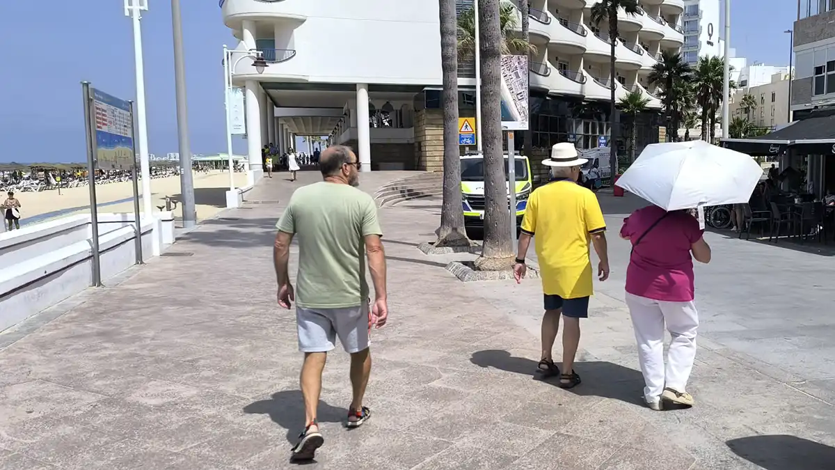 Una mujer camina bajo un parasol junto a un hombre por el paseo marítimo de Cádiz en estos días de calor.