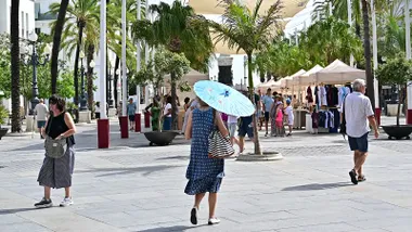 Una mujer camina con un parasol por la plaza de San Juan de Dios de Cádiz.