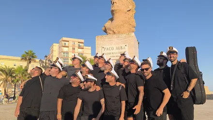 La chirigota de vera Luque posa con gorra marinera al estilo Paco Alba ante su busto antes de interpretar la copla de Currusquillos Gaditanos.