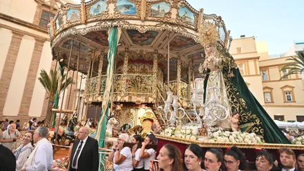 La virgen de las Cigarreras, en parihuela, pasa delante del tiovivo en su llegada en la tarde de ayer a la Catedral