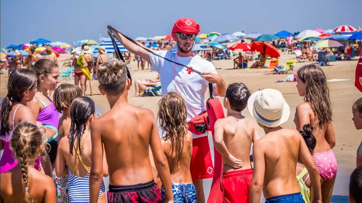 Socorrista con camiseta blanca y cruz rojo junto a niños y niñas.