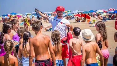 Socorrista con camiseta blanca y cruz rojo junto a niños y niñas.