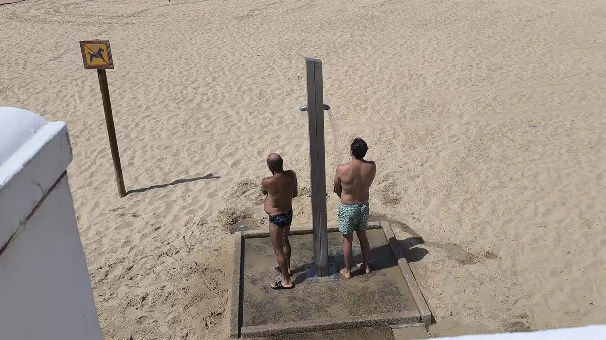 Dos hombres toman una ducha en la playa de la Victoria de Cádiz