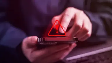 Mano de una persona con un móvil con el signo de precaución.