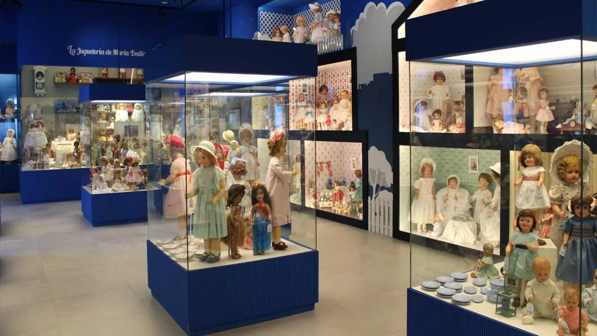 Muñecas en el marco de la exposición, dentro de vitrinas y destacando el color azul.