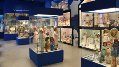Muñecas en el marco de la exposición, dentro de vitrinas y destacando el color azul.
