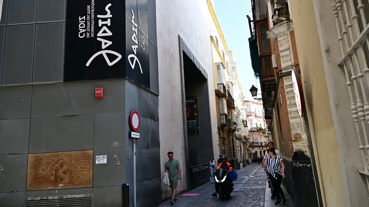 Imagen exterior del Yacimiento Arqueológico Gadir, con su cartel identificativo en la fachada y varias personas paseando por la calle.
