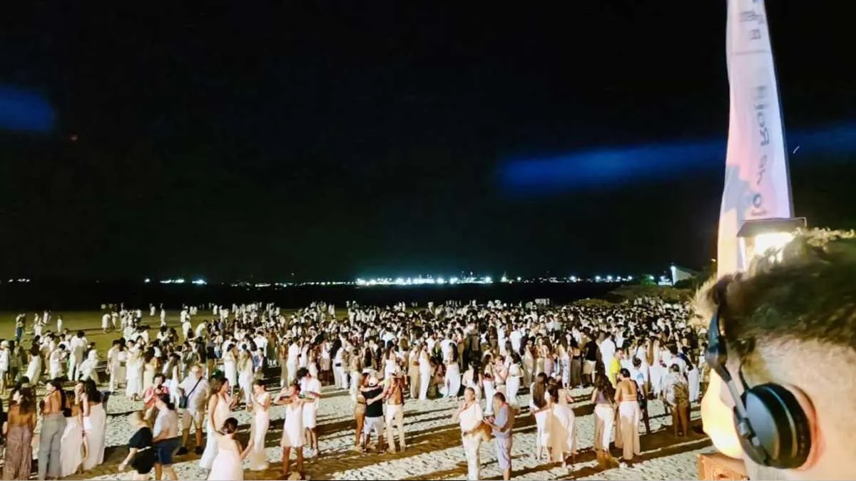 Personas bailando en la playa de Roya y un DJ con cascos de música puestos.