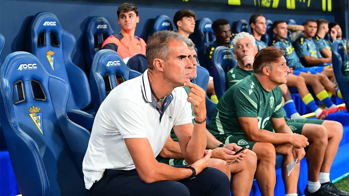 El entrenador del Cádiz CF, Gaizka Garitano, aparece sentado en el banquillo del Nuevo Mirandilla durante el Trofeo Carranza. Viste el chándal oficial del club y mantiene una expresión pensativa y seria, con la mirada fija hacia el terreno de juego.