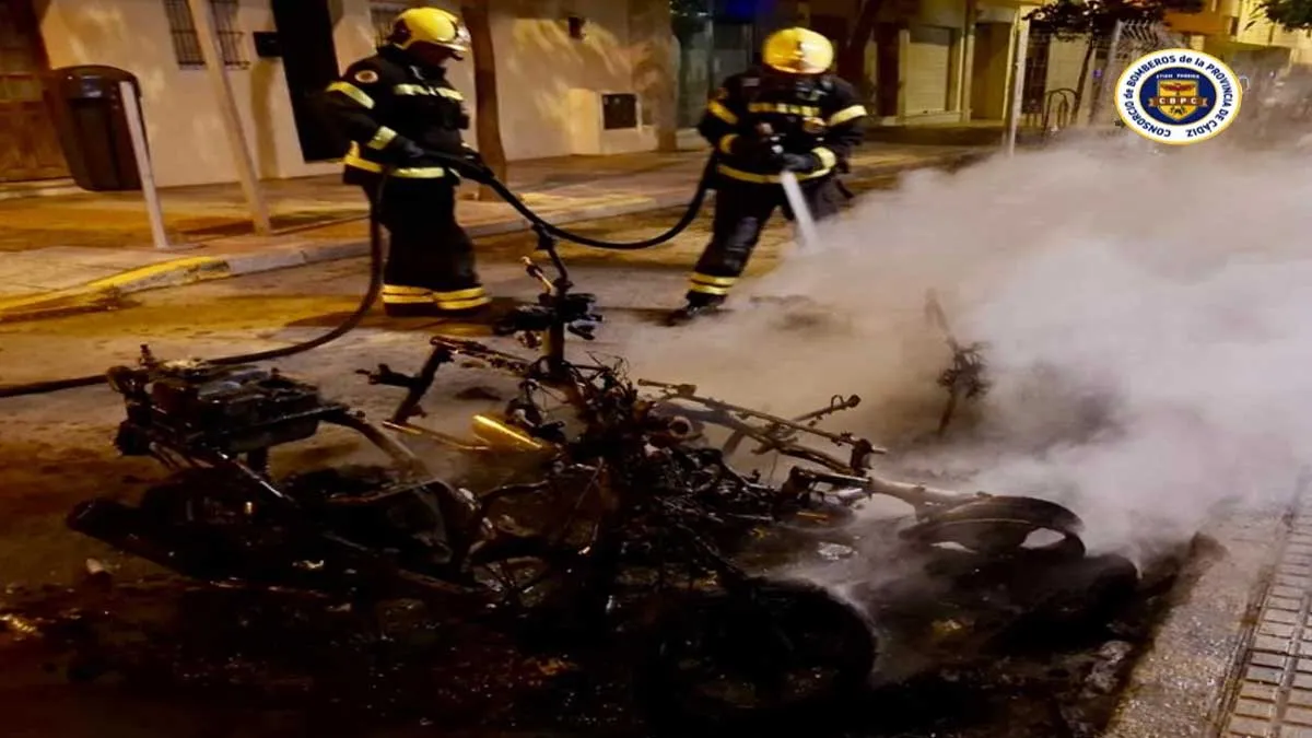Dos bomberos apagan el fuego, están junto al chasis calcinado de una moto.