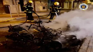 Dos bomberos apagan el fuego, están junto al chasis calcinado de una moto.