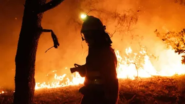 Bosque en llamas y silueta de un bombero.