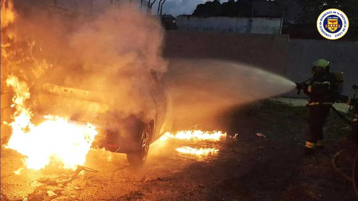 Bombero apagando vehículo envuelto en llamas.
